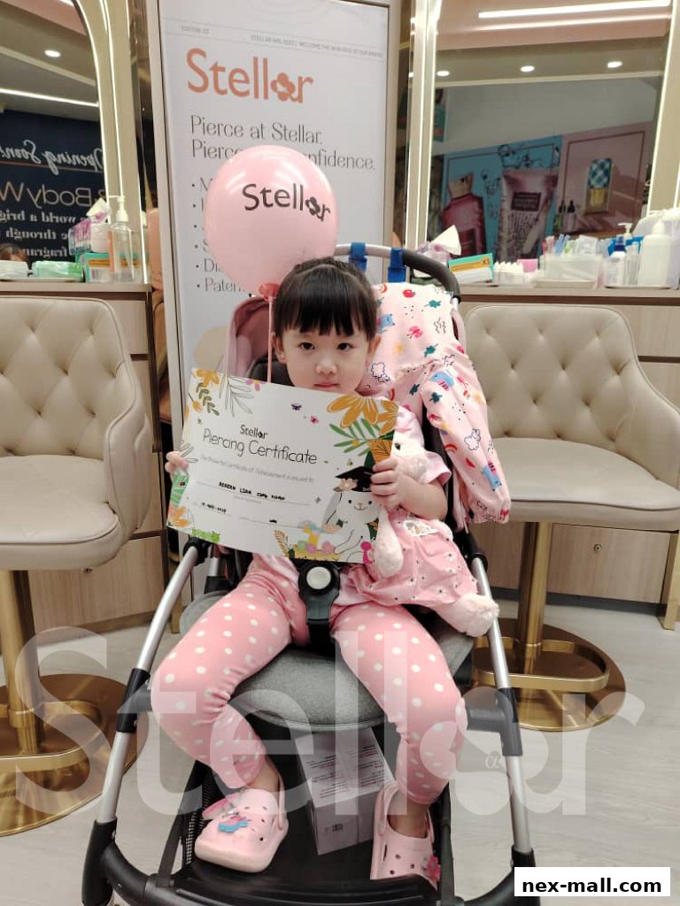 A young child holds a piercing certificate and a Stellar balloon in a stroller.
