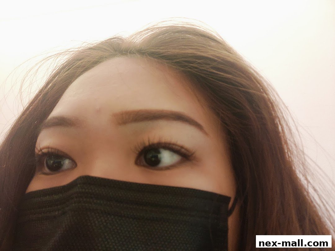 A close-up of a woman's eyes and forehead, wearing a black face mask and showing off her eyelash extensions.