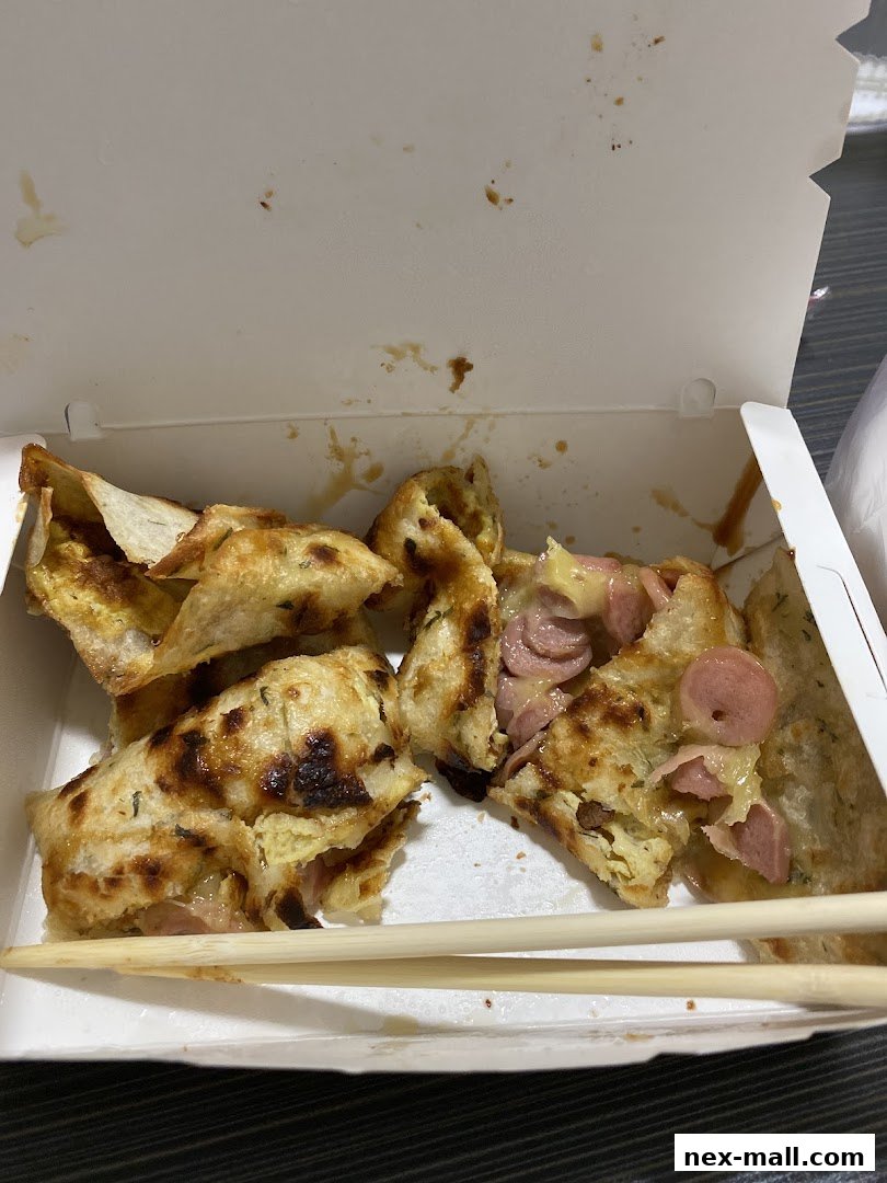 A white takeout box filled with Taiwanese street snacks, featuring savory crepes with sausage and egg.