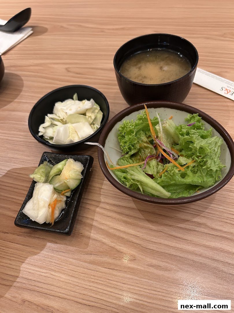 A Japanese meal featuring miso soup, a fresh salad, and assorted pickles on a wooden table.