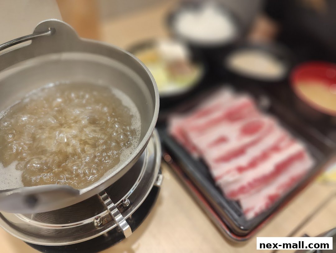 A close-up of a pot of boiling broth with thinly sliced meat ready for cooking.