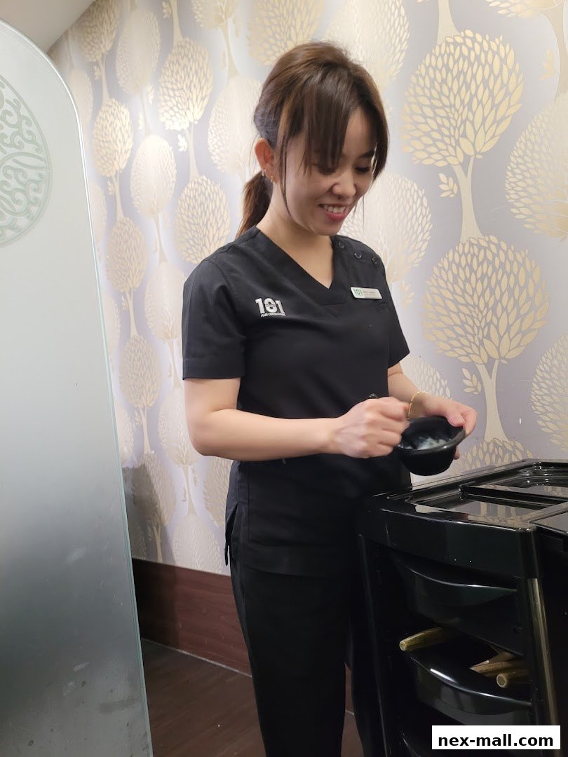 A smiling woman in a black uniform holds a bowl while standing next to a salon trolley.