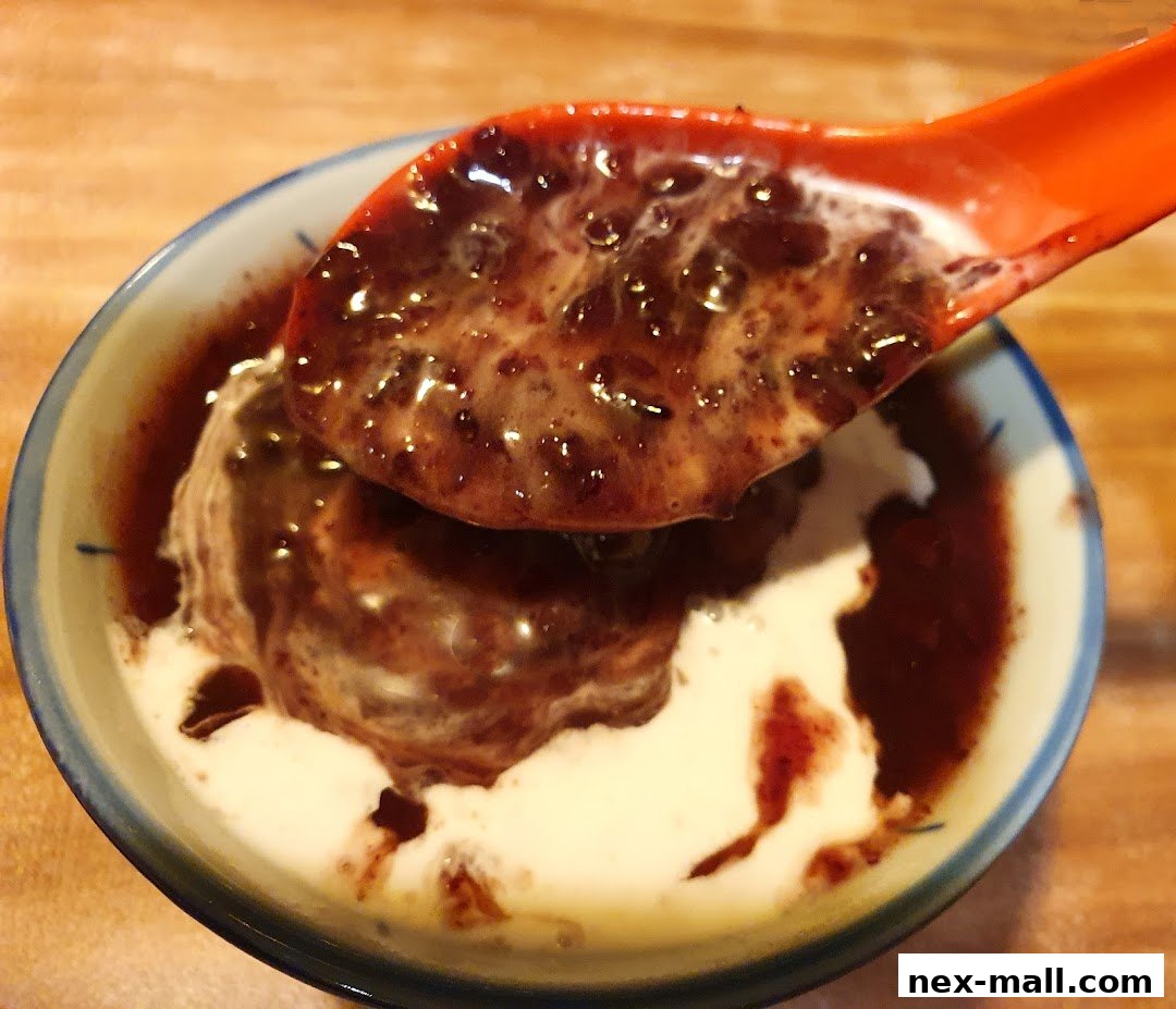 A spoonful of black rice dessert with coconut milk is being lifted from a bowl.
