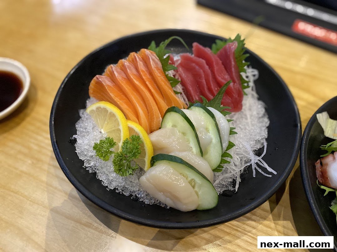 A plate of fresh sashimi with salmon, tuna, and scallops, garnished with lemon and cucumber.