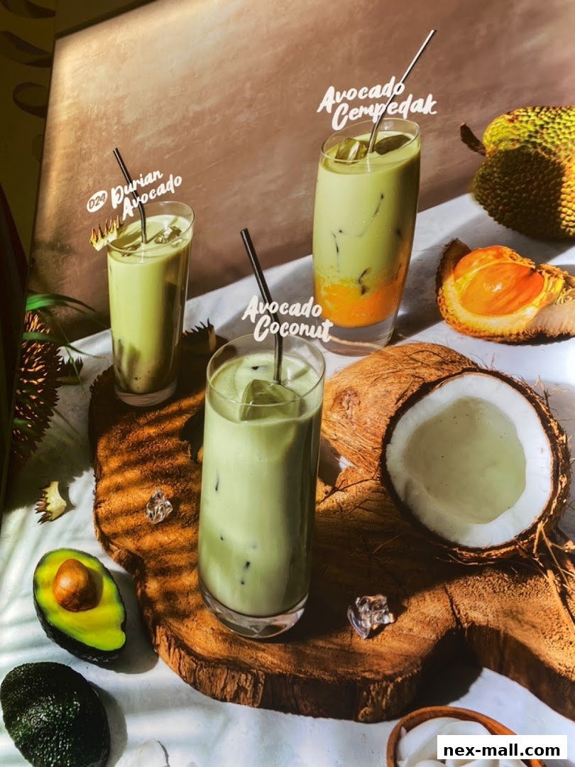 Three refreshing avocado-based drinks with fresh fruits and ice on a wooden board.