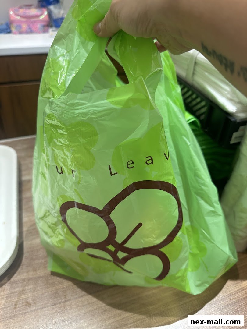A hand holds a bright green shopping bag with the "Four Leaves" logo and clover pattern.