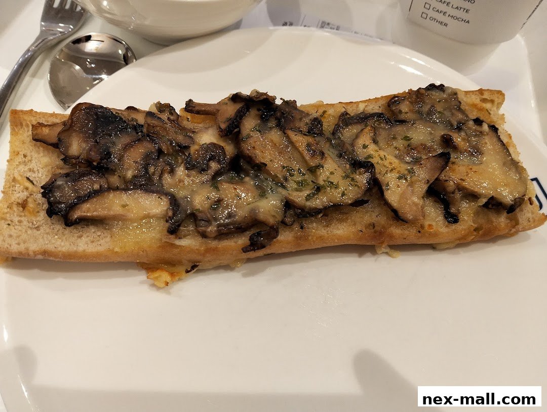 A close-up of a mushroom and cheese open-faced sandwich on a white plate.