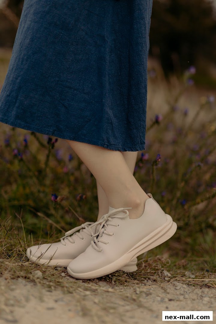 A person wearing light-colored sneakers and a blue dress stands in a grassy area with flowers.