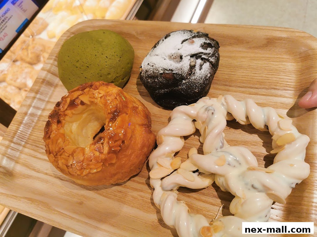 A wooden tray holds four delicious Japanese pastries, including a green tea bun and a chocolate pastry.