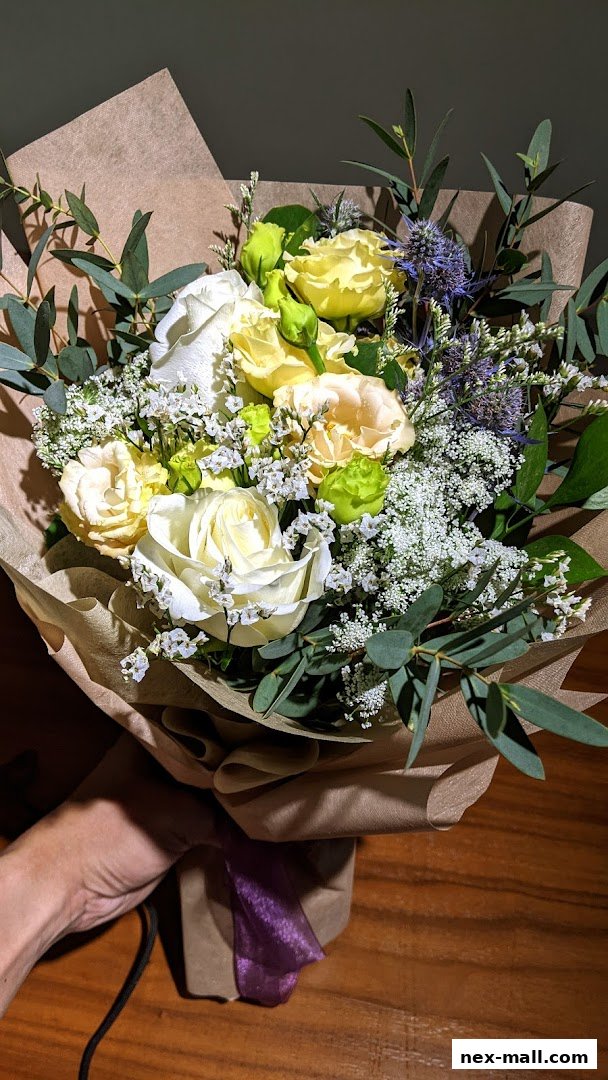 A hand holding a beautifully arranged bouquet of white and yellow roses with eucalyptus.
