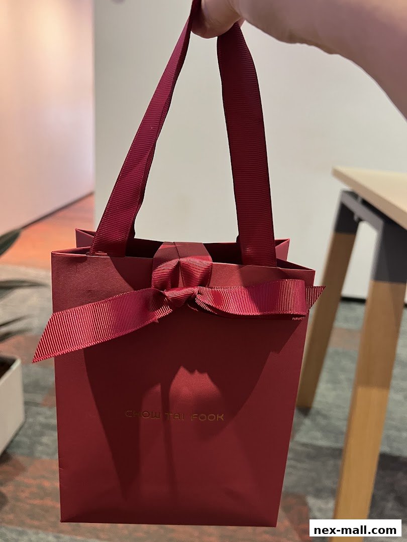 A hand holds a red gift bag with a ribbon bow from Chow Tai Fook Jewellery.