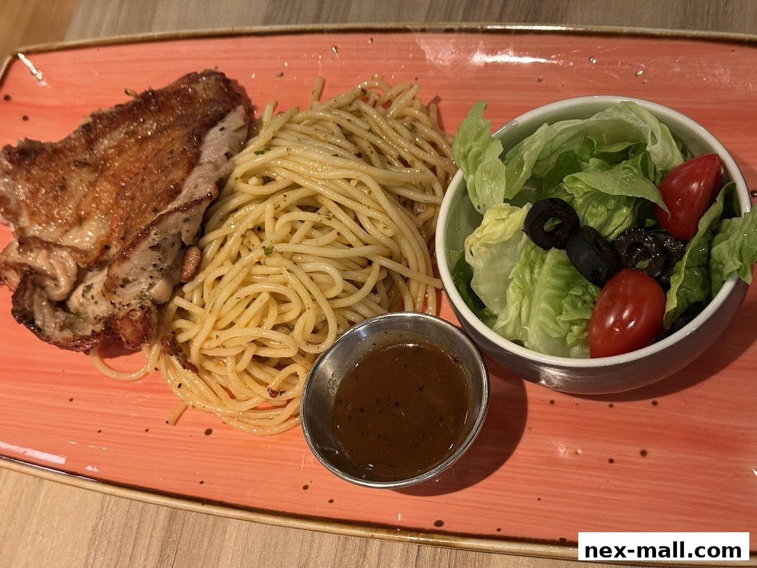 A plate of spaghetti with grilled chicken and a side salad with cherry tomatoes and olives.