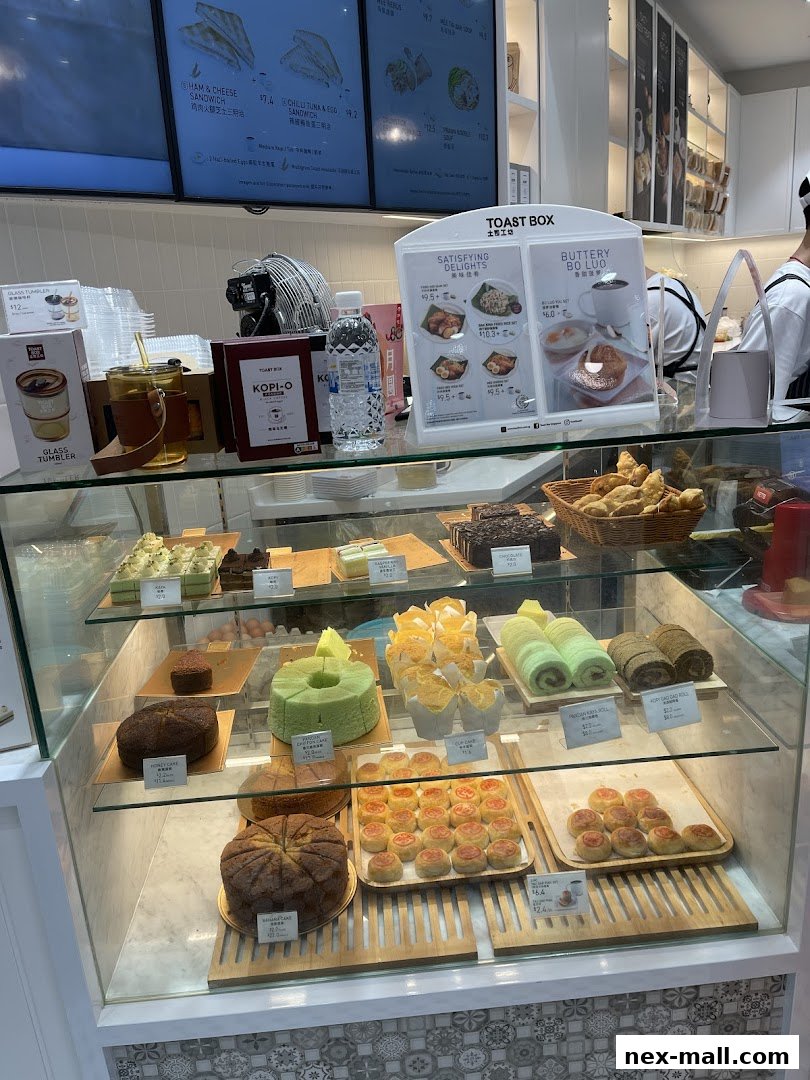 A display case filled with various cakes, pastries, and bread at Toast Box.