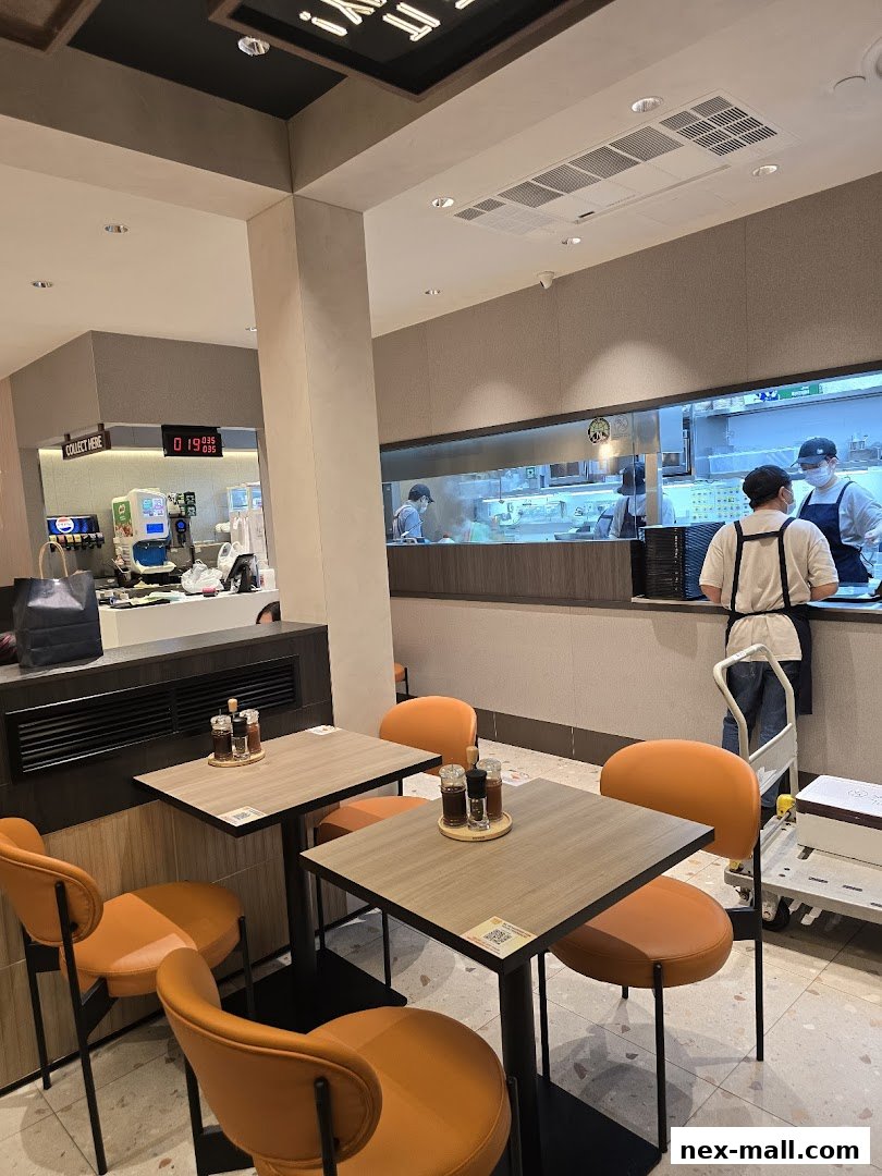 Interior view of Pepper Lunch with tables, chairs, and kitchen staff working.