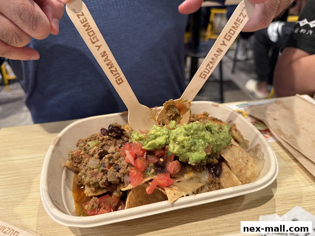 A person holds wooden cutlery over a bowl of nachos with guacamole, salsa, beans, and meat.