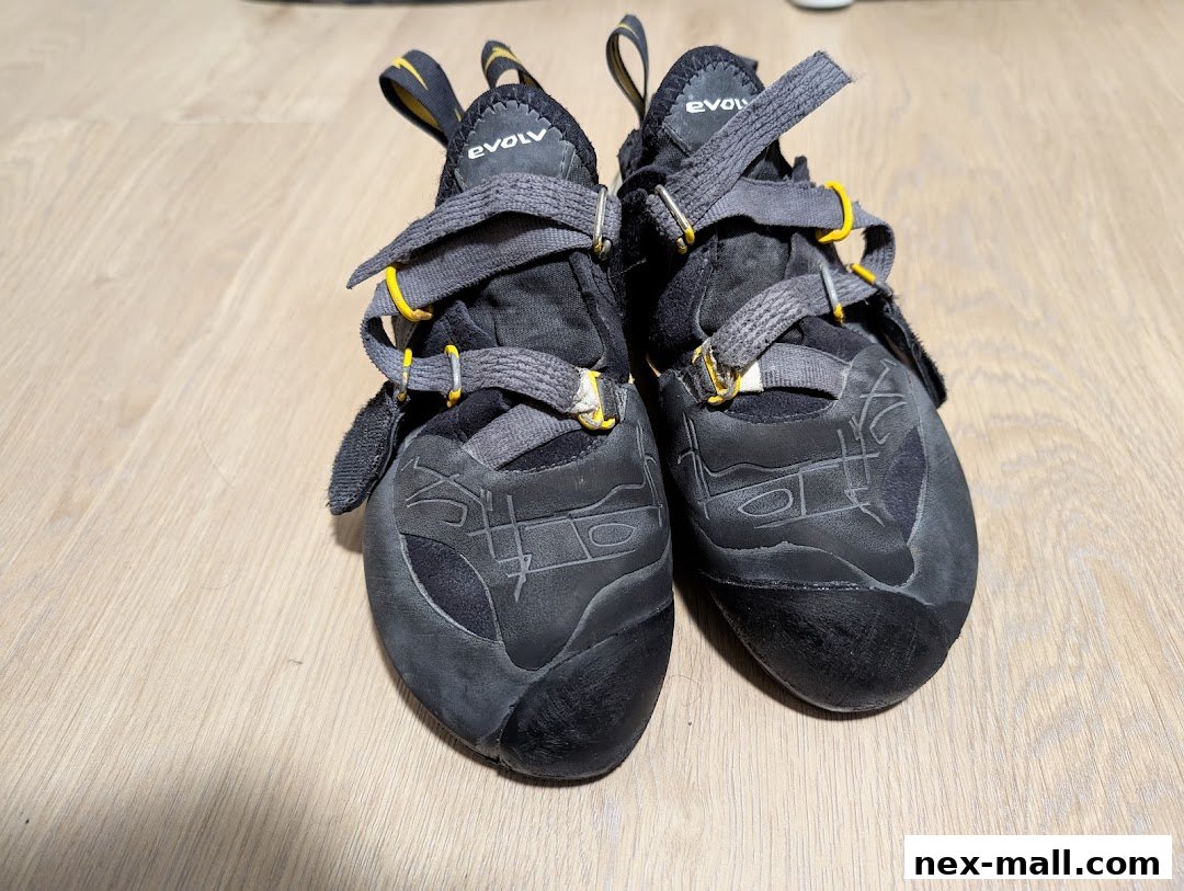 A pair of black climbing shoes with grey laces and yellow accents on a wooden floor.