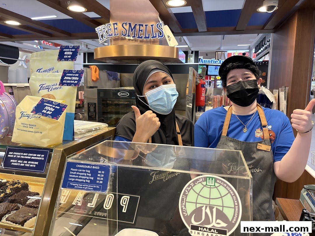 Two smiling staff members at Famous Amos, giving thumbs up, with cookies and bags displayed.