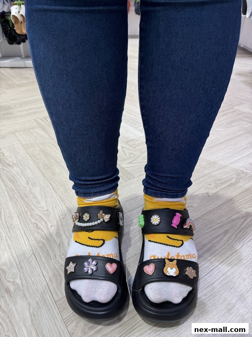A person wearing Crocs sandals adorned with various colorful Jibbitz charms and character socks.