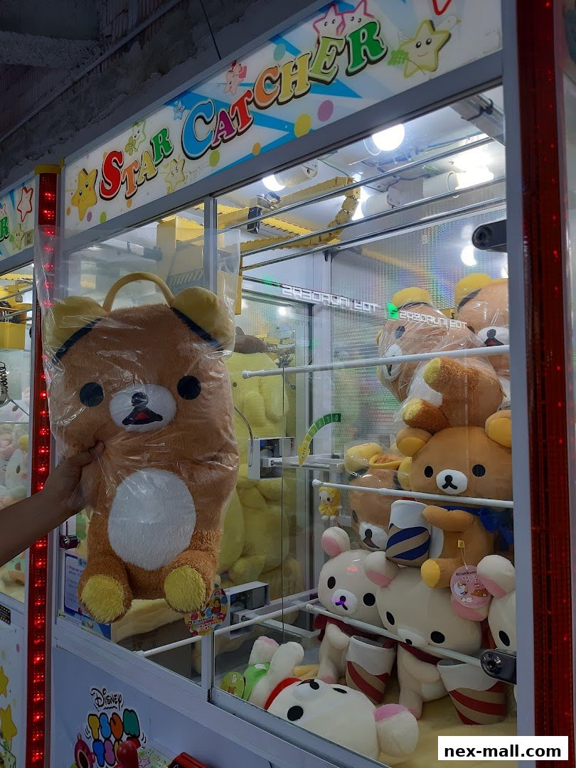 A hand reaches into a claw machine filled with plush toys, including Rilakkuma characters.