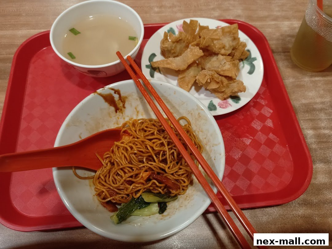 A close-up of a meal with noodles, soup, fried wontons, and a drink on a red tray.