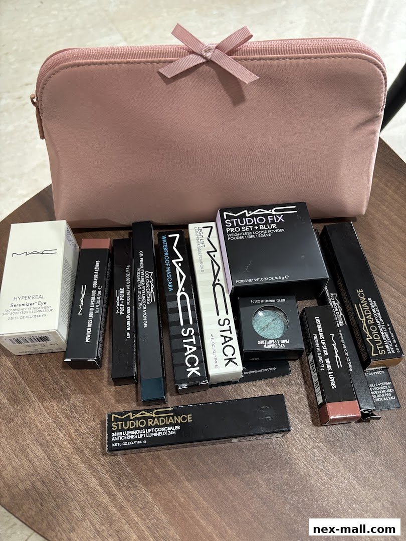 A collection of MAC Cosmetics makeup products, including foundation, lipstick, and eye shadow, arranged with a pink makeup bag.