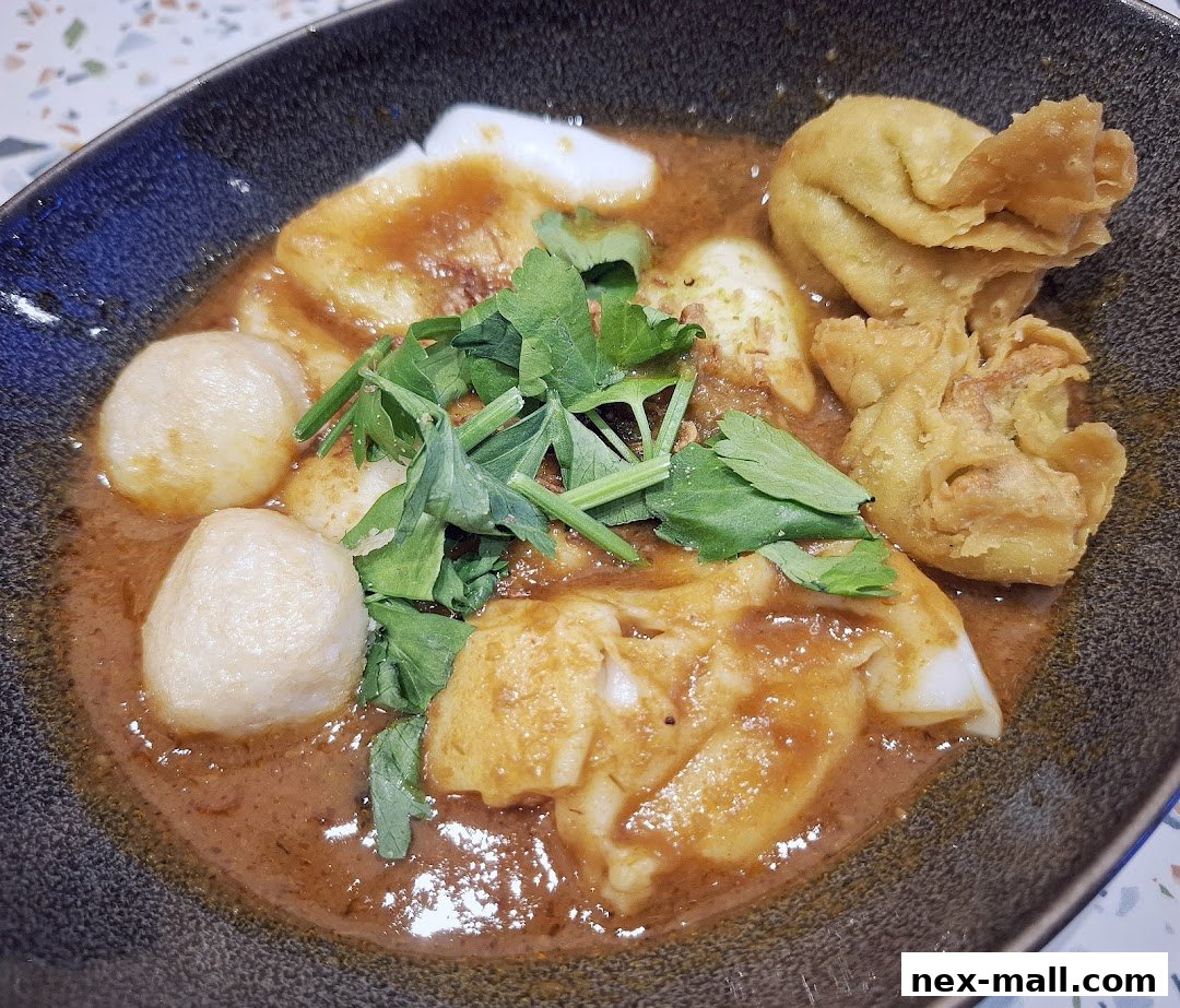 A close-up shot of a delicious bowl of Hainanese curry noodles with fish balls and wontons.