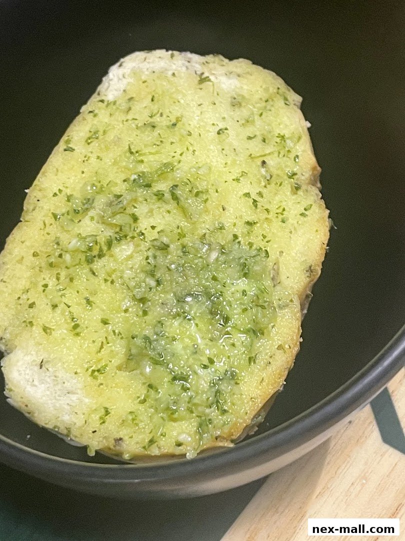A close-up shot of a slice of garlic bread with herbs in a dark bowl.
