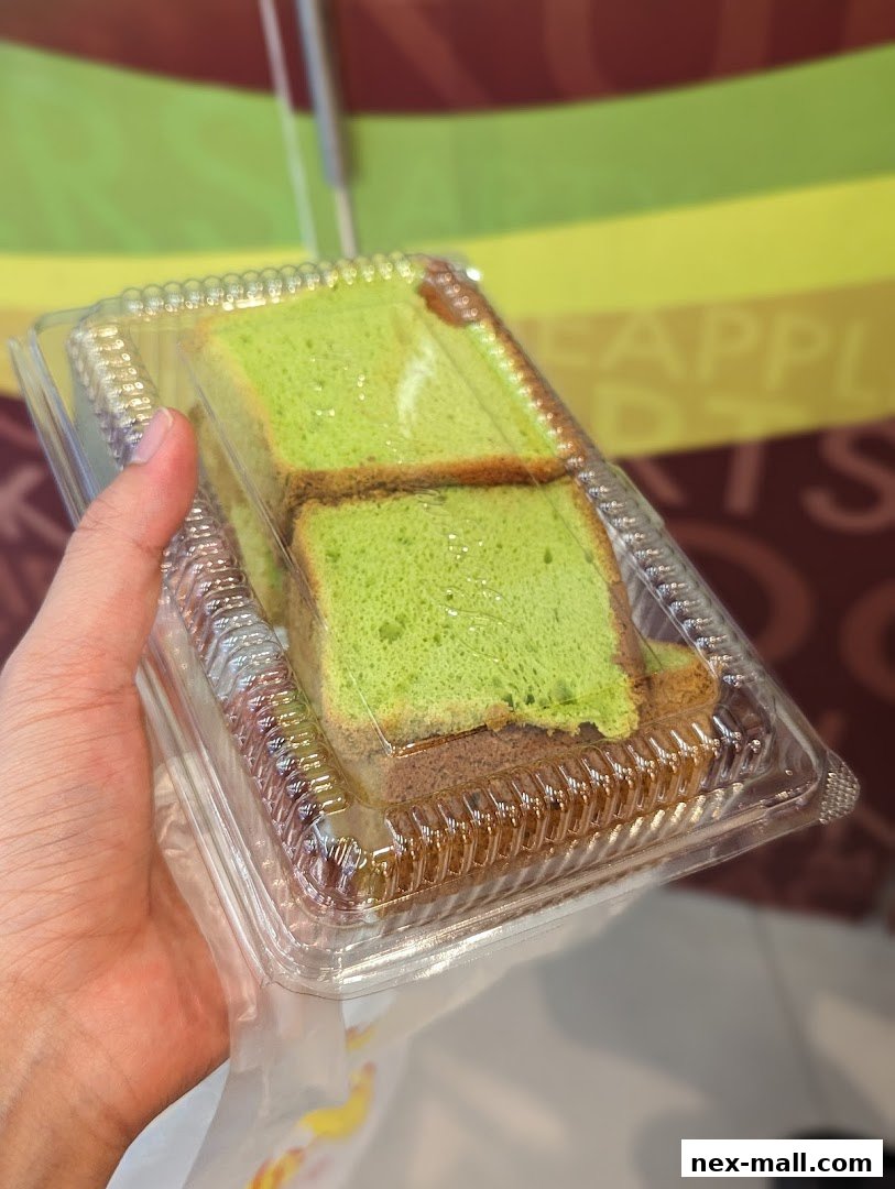 A hand holds a clear plastic container with slices of green pandan cake.