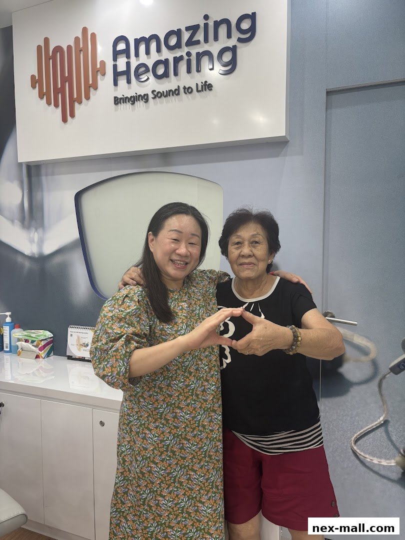 Two women smiling and making a heart shape with their hands in front of an Amazing Hearing sign.