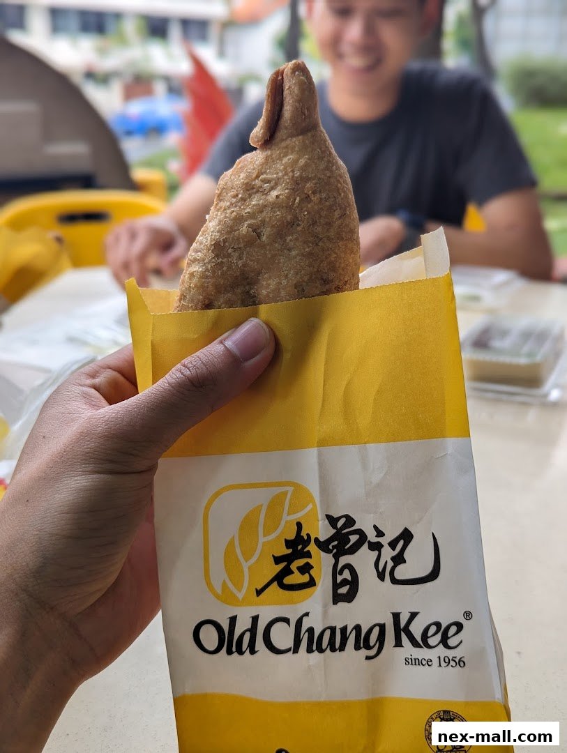 A hand holds a crispy fried snack from Old Chang Kee, with a smiling person in the background.