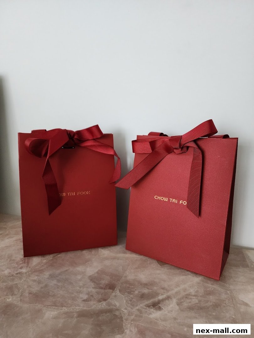 Two red gift bags with gold lettering and red ribbon bows from Chow Tai Fook Jewellery.