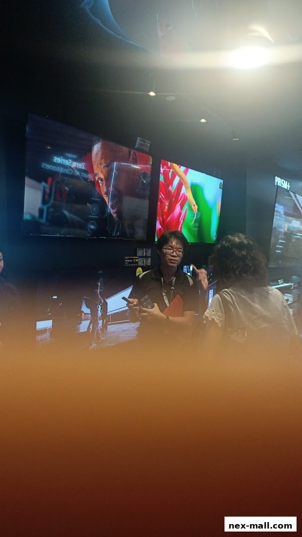 A store employee demonstrates products to a customer in front of large screens.