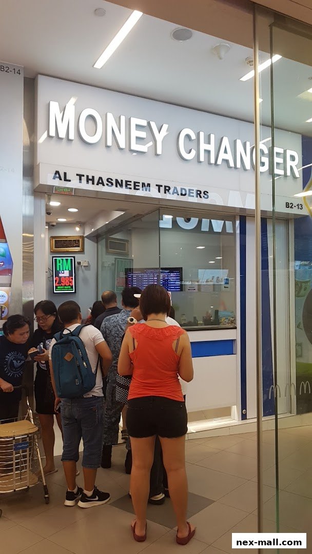 People queuing outside a money changer shop with a prominent sign.