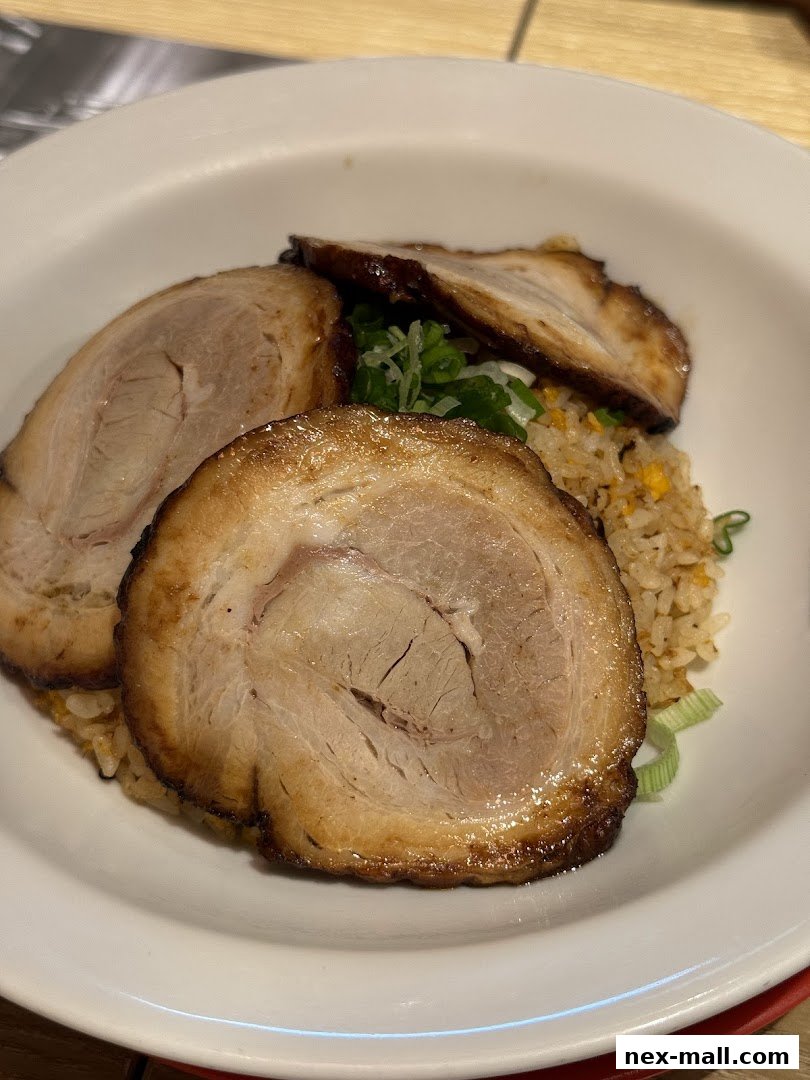 A close-up of a bowl of ramen with thick slices of chashu pork and fried rice.