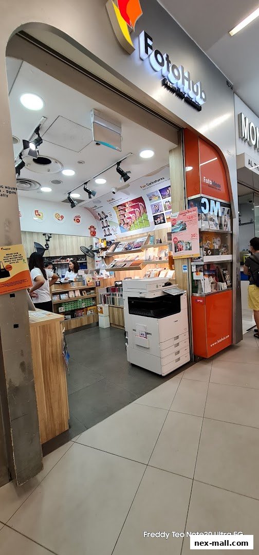 The entrance of FotoHub, a shop offering photo services and products, with displays and a printer visible.