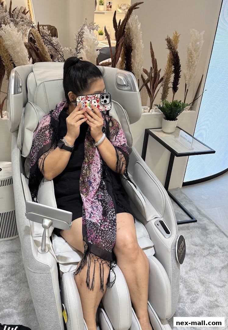 A woman sits in a luxurious massage chair, holding her phone up to her face.