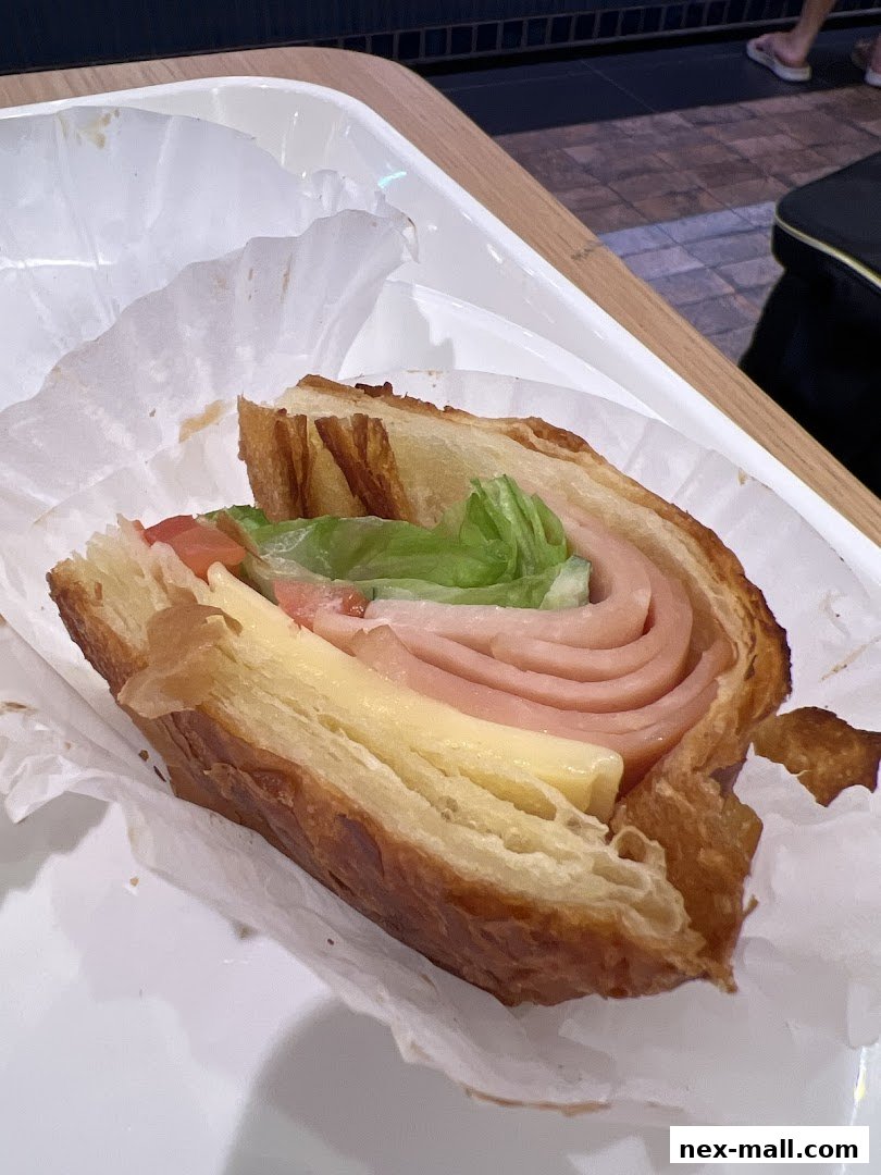 A close-up of a ham and cheese sandwich on a flaky croissant.