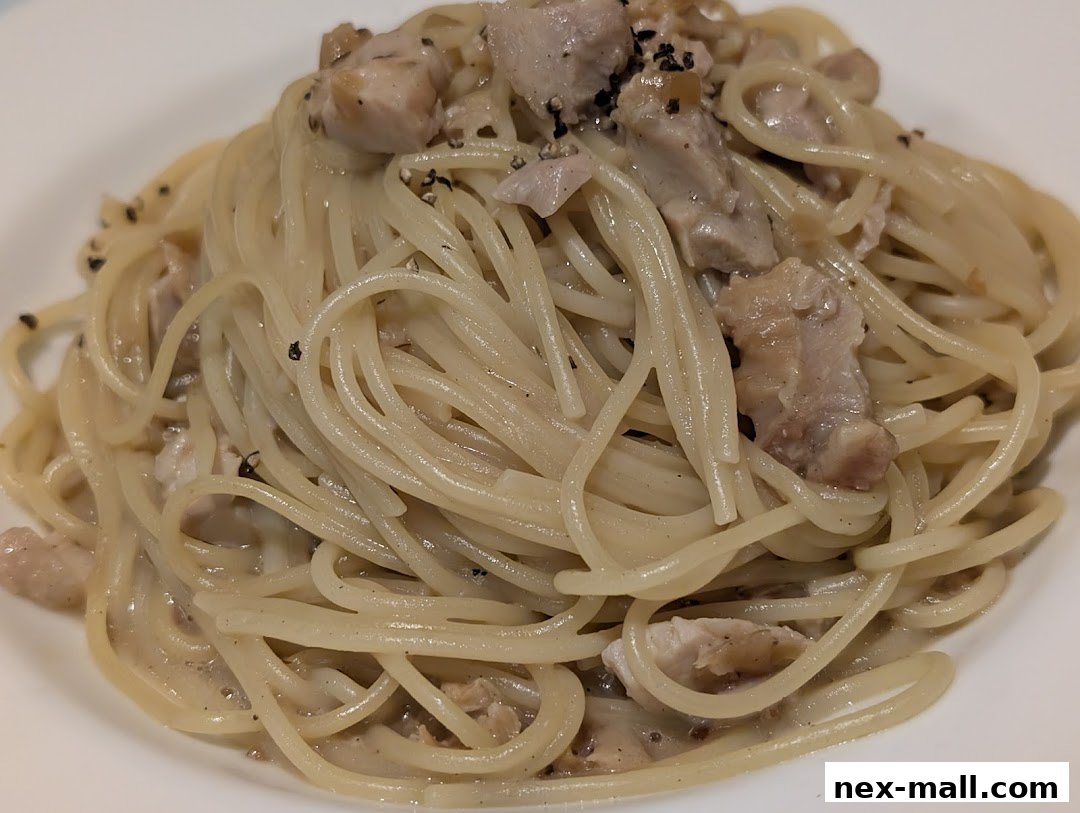 A close-up shot of a creamy pasta dish with chicken pieces and black pepper.