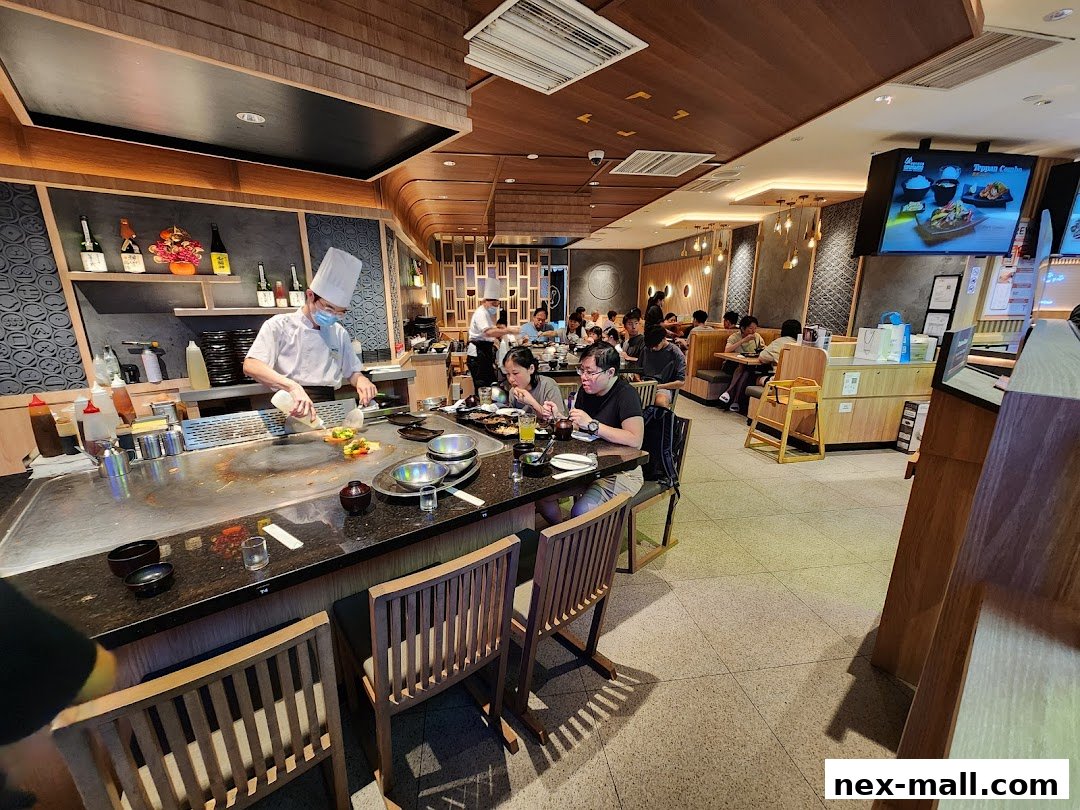 A chef prepares food on a teppanyaki grill while diners eat at tables in a restaurant.