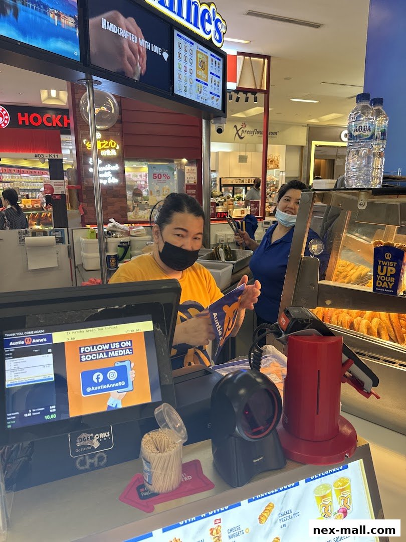 Two staff members at an Auntie Anne's pretzel counter, with a POS system and pretzels visible.