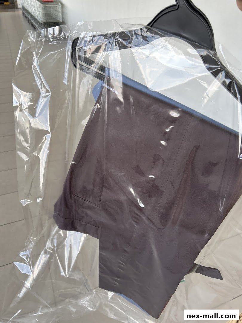A pair of dark trousers on a hanger, covered in plastic, ready for laundry service.
