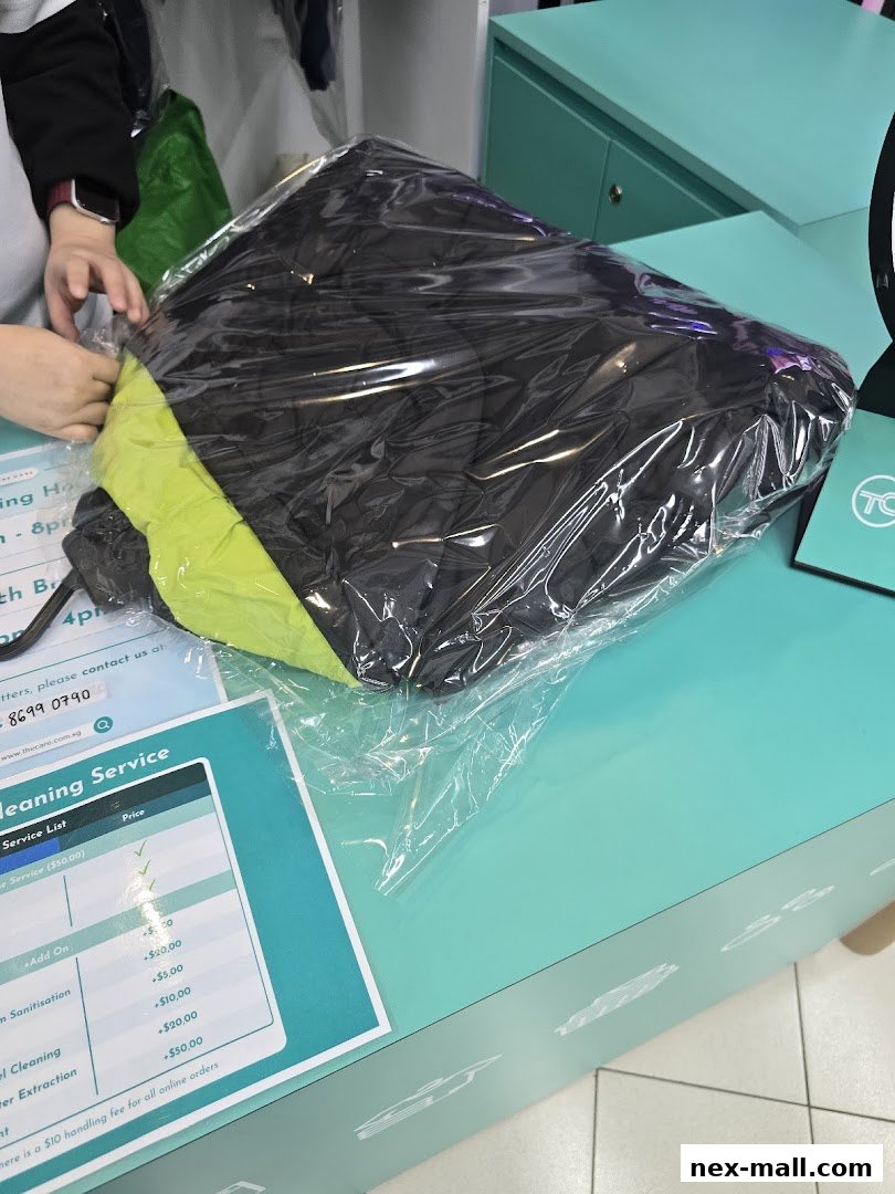 A person is packaging a black and green jacket in plastic wrap at a counter.