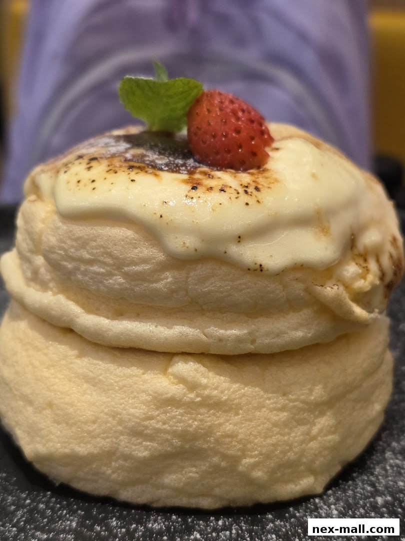 A close-up of fluffy soufflé pancakes topped with cream, a strawberry, and mint.