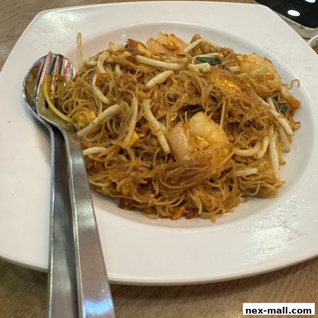 A plate of stir-fried noodles with shrimp and bean sprouts, served with cutlery.