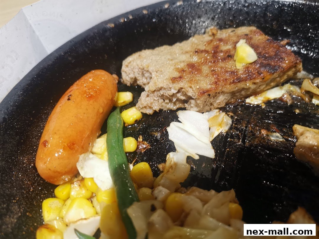 A sizzling hot plate with a hamburger steak, sausage, corn, and vegetables.