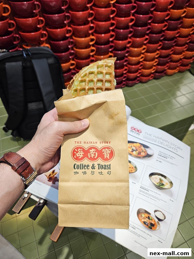 A hand holds a waffle in a paper bag from The Hainan Story Coffee & Toast.