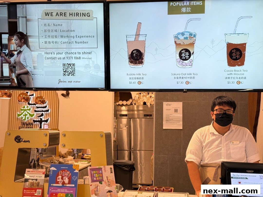 A shop counter with popular bubble tea drinks displayed on a screen and a staff member.