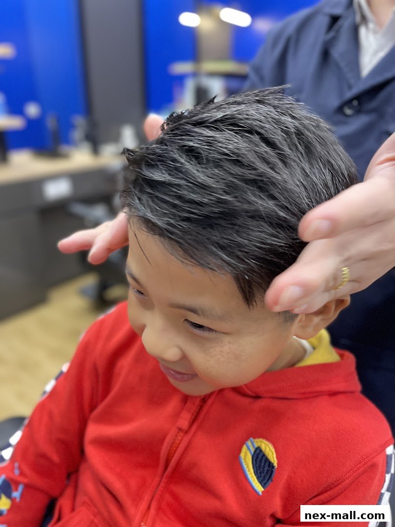A young boy with dark hair is getting his hair styled by a barber.