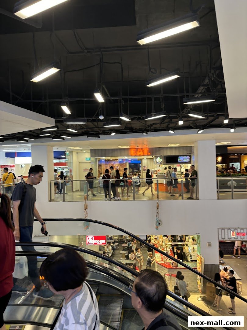 People are seen queuing at the 'EAT.' food stall on the upper level of a mall.