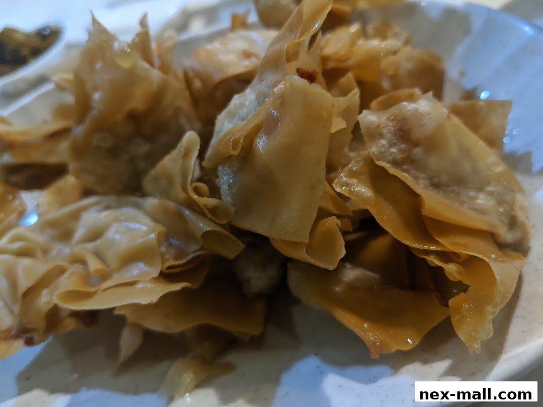 A close-up shot of crispy, golden-brown fried wontons served on a white plate.